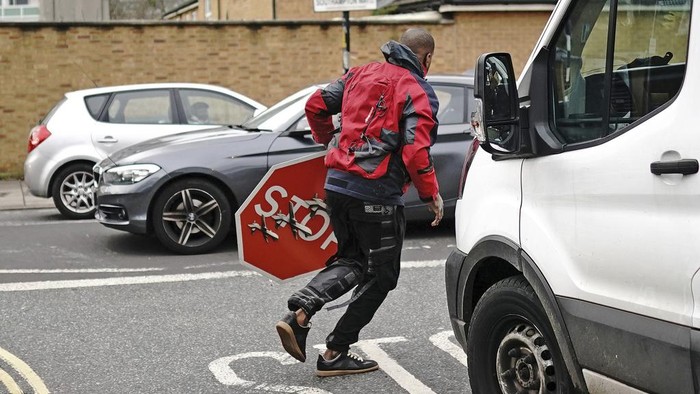 A person removes a piece of art work by Banksy, which shows what looks like three drones on a traffic stop sign, which was unveiled at the intersection of Southampton Way and Commercial Way in Peckham, south east London, Friday Dec. 22, 2023. (Aaron Chown/PA via AP)