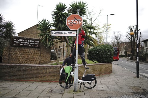 A person removes a piece of art work by Banksy, which shows what looks like three drones on a traffic stop sign, which was unveiled at the intersection of Southampton Way and Commercial Way in Peckham, south east London, Friday Dec. 22, 2023. (Aaron Chown/PA via AP)
