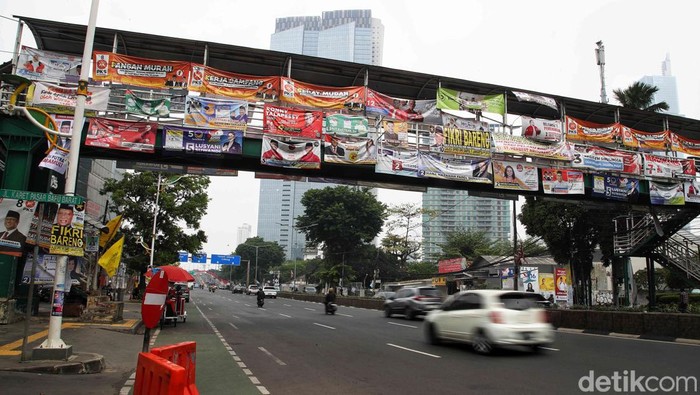 Kendaraan melintas di bawah Jembatan Penyeberangan Orang (JPO) yang tertutup oleh alat peraga kampanye Pemilu 2024 di Jalan KH Mas Mansyur, Tanah Abang, Jakarta Pusat, Rabu (27/12/2023).