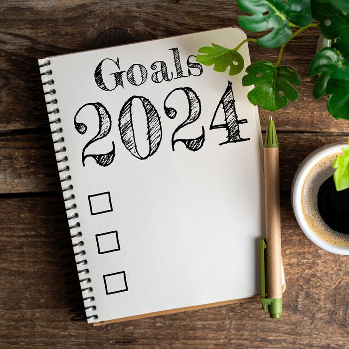 New year goals 2024 on desk. 2024 resolutions list with notebook, coffee cup on table. Goals, resolutions, plan, action, checklist concept. New Year 2024 template, copy space