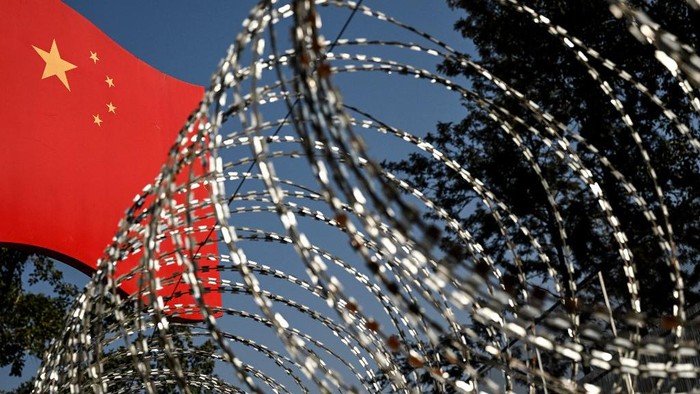 This photograph taken on January 14, 2023, shows a part of a border wall between China and Myanmar with barbed wire and a Chinese national flag, in Ruili, west Yunnan Province. The city of Ruili is slowly creaking back to life as China ditches its zero-tolerance Covid strategy after years of strict lockdowns and other gruelling restrictions. (Photo by Noel CELIS / AFP)