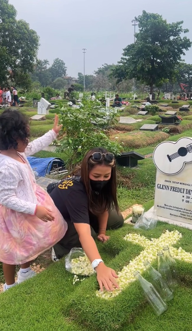 Gewa juga ikut memberikan bunga melati ke atas makam yang dibantu Mutia Ayu. Mutia Ayu terlihat mengenakan baju kasual berupa kaos hitam dan celana cargo. Foto: Instagram @mutia_ayuu