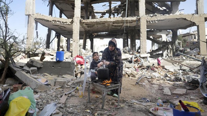 Palestinian woman Hiyam Qudih cooks in front of her familys building destroyed in the Israeli bombardment of the Gaza Strip in the village of Khuzaa, east of Khan Younis, Gaza Strip, Sunday, Nov. 26, 2023. on the third day of the temporary ceasefire between Hamas and Israel. (AP Photo/Adel Hana)