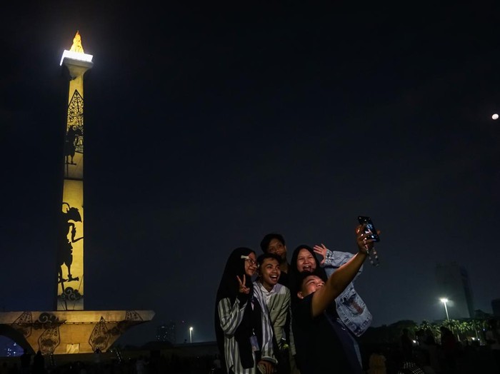 Pengunjung menyaksikan pertunjukan video pemetaan Monas Week di Monumen Nasional, Jakarta, Kamis (28/12/2023). Pertunjukan yang akan berlangsung hingga 31 Desember 2023 itu untuk menghibur dan memeriahkan liburan akhir tahun dengan menampilkan tema Natal, liburan sekolah, dan tahun baru. ANTARA FOTO/Rifqi Raihan Firdaus/tom.