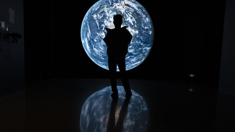 A visitor stands near a display showing earth during an exhibition about China's space program in Beijing, Thursday, Dec. 28, 2023. China's burgeoning space program plans to place astronauts on the moon before 2030 and expand the country's orbiting space station against the background of a rivalry with the U.S. for reaching new milestones in outer space, reflecting their competition for influence on global events. (AP Photo/Ng Han Guan)