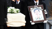 Anak laki-laki Lee Sun Kyun membawa foto sang ayah ketika peti mati berisi jenazah sang aktor Parasite dibawa keluar dari rumah duka. (Foto: STR / KOREA POOL / AFP)