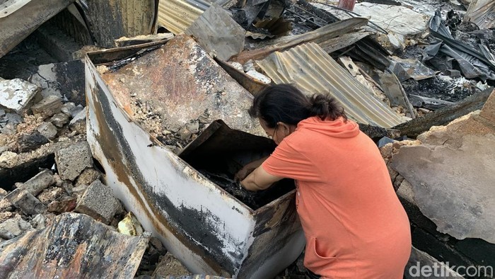 Seorang warga saat mengais sisa-sisa dari puing bangunan yang hangus dibakar massa pengantar jenazah Lukas Enembe.