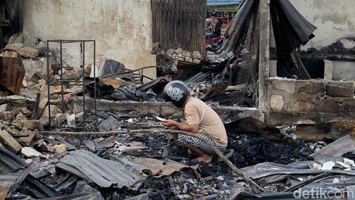 Seorang warga saat mengais sisa-sisa dari puing bangunan yang hangus dibakar massa pengantar jenazah Lukas Enembe.
