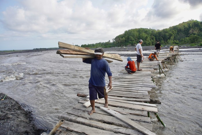 Sejumlah warga mengangkat kayu untuk dipasang di jembatan kayu yang rusak di daerah aliran sungai (DAS) Gunung Semeru, Desa Lebakharjo, Ampelgading, Malang, Jawa Timur, Sabtu (30/12/2023). Jembatan swadaya masyarakat sepanjang 100 meter yang digunakan sebagai jalan alternatif antar desa itu dapat memotong jarak tempuh hingga 14 kilometer, rusak akibat diterjang arus sungai setelah hujan. ANTARA FOTO/Irfan Sumanjaya/Spt.