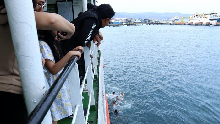 Penumpang kapal penyeberangan melempar uang ke laut yang akan diperebutkan anak logam di Pelabuhan Ketapang Banyuwangi, Jawa Timur, Senin (1/1/2024). Meskipun sudah dilarang oleh pihak pelabuhan karena dapat membahayakan diri serta pelayaran kapal, namun atraksi anak logam menjadi tontonan dan hiburan bagi penumpang kapal selama masa libur Tahun Baru 2024. ANTARA FOTO/Budi Candra Setya/foc.