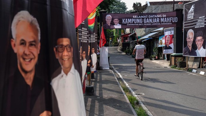 Kampung Ganjar Mahfud di Solo Warga melewati poster pasangan Capres dan Cawapres nomor urut 3 Ganjar Pranowo dan Mahfud MD yang dipajang di Kampung Ganjar Mahfud, Kelurahan Pajang, Kecamatan Laweyan, Solo, Jawa Tengah, Senin (1/1/2024). Kampung tersebut diresmikan untuk sosialisasi program kerja pasangan Capres dan Cawapres nomor urut 3 Ganjar Pranowo dan Mahfud MD guna memenangkan Pemilu Presiden pada Februari 2024 mendatang. ANTARAFOTO/Maulana Surya/foc.