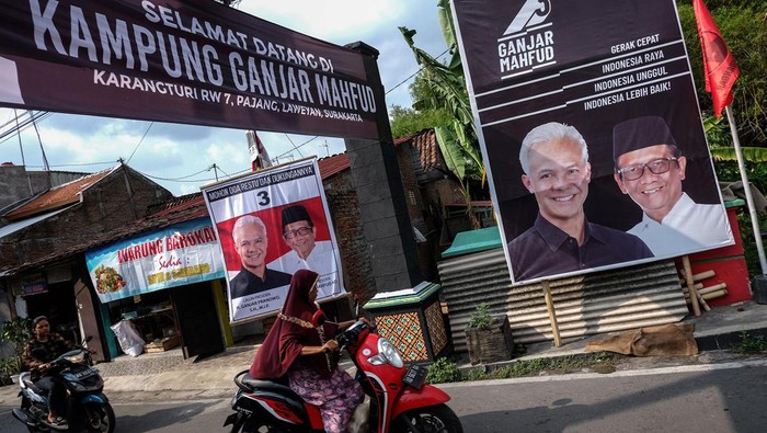 Kampung Ganjar Mahfud di Solo Warga melewati poster pasangan Capres dan Cawapres nomor urut 3 Ganjar Pranowo dan Mahfud MD yang dipajang di Kampung Ganjar Mahfud, Kelurahan Pajang, Kecamatan Laweyan, Solo, Jawa Tengah, Senin (1/1/2024). Kampung tersebut diresmikan untuk sosialisasi program kerja pasangan Capres dan Cawapres nomor urut 3 Ganjar Pranowo dan Mahfud MD guna memenangkan Pemilu Presiden pada Februari 2024 mendatang. ANTARAFOTO/Maulana Surya/foc.