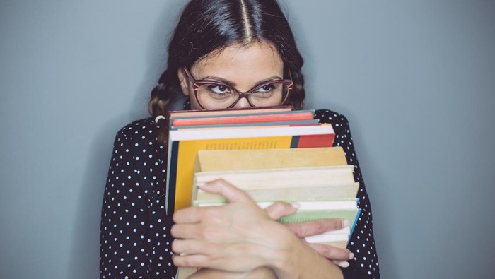 Evil bookworm hiding behind a top of books - ilustrasi introvert
