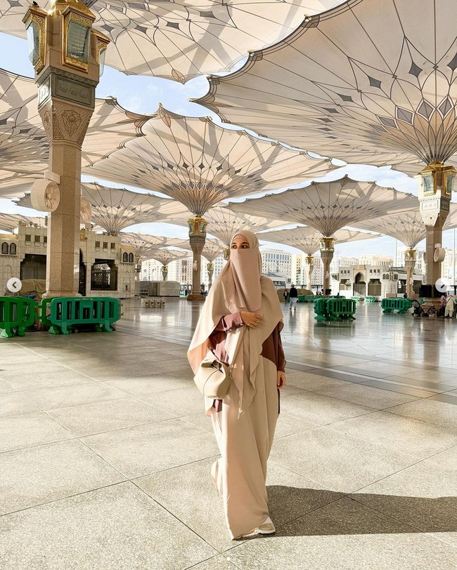 Shireen Sungkar menjalani ibadah umrah bersama suaminya, Teuku Wisnu dan anak pertamanya Teuku Adam Al Fatih. Shireen berada di Tanah Suci sejak 24 Desember 2023 hingga Tahun Baru 2024 ini. Shireen terlihat memakai cadar, abaya dan french khimar warna latte dari @geraihawa saat berpose di halaman Masjid Nabawi.  Foto: Dok. Instagram @shireensungkar.