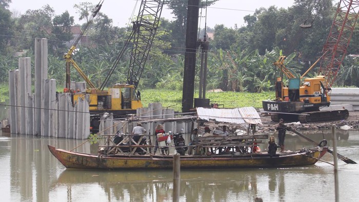Progres Jembatan Jongbiru yang Jadi Akses Bandara Kediri Besutan Gudang Garam Warga menggunakan perahu penyeberangan dengan latar belakang proyek pembangunan Jembatan Jongbiru di Sungai Brantas, Kediri, Jawa Timur, Rabu (3/1/2024). Proyek pembangunan jembatan sepanjang 133 meter sebagai penghubung kota dengan kabupaten Kediri sekaligus jalur penyangga menuju Bandara Dhoho Kediri tersebut ditargetkan selesai pada Mei 2024. ANTARA FOTO/Prasetia Fauzani/rwa.