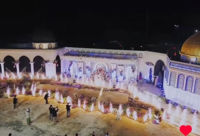 Dalam unggahannya, makeup artist itu juga memperlihatkan luasnya arena pesta pernikahan tema Palestina ini. Tampak pernikahan digelar indoor dan outdoor. Pelaminannya didekorasi cantik bernuansa putih dengan lampu sorot warna ungu. Ada juga hiasan kembang api yang mengelilingi sekitar pelaminan. Foto: Dok. Permana Fotografer.