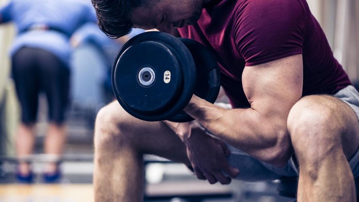 Muscular young man doing exercises for biceps muscles with dumbbells on in a gym.