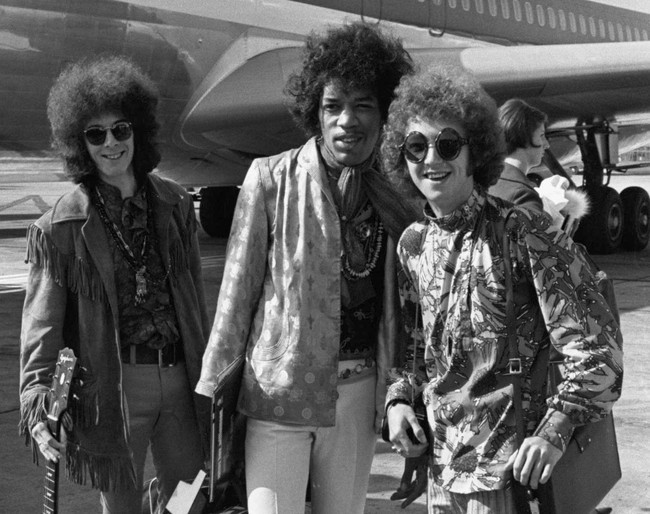 Perubahan juga ditandai dengan euforia budaya pop yang melahirkan tren glamrock yang flamboyan. Sejumlah musisi mempelopori gaya tersebut di antaranya pemain bas Noel Redding, gitaris Jimi Hendrix, dan drummer Mitch Mitchell, seperti yang terlihat ketika mereka dipotret di Bandara Heathrow, London, Inggris, pada 1967. (Foto: AP/Peter Kemp)