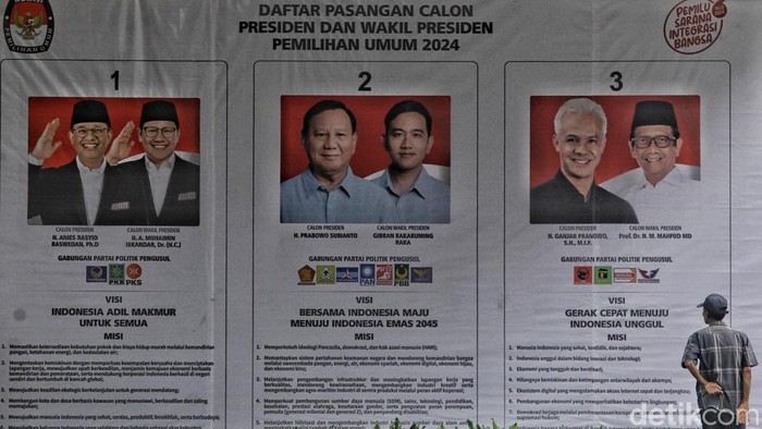 Warga melintas di depan baliho yang menayangkan kertas suara dalam ukuran jumbo dan berisi visi dan misi tiga pasangan calon presiden dan wakil presiden 2024 di kawasan Kuningan, Jakarta, Selasa (9/1/2024).