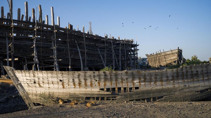 Melihat Pembuatan Kapal Tradisional di India Dogs sleep next to a discarded boat in the foreground at a site where two traditional ships are under construction in Mandvi in Gujarat, India, Tuesday, Jan. 9, 2024. This 400-year-old tradition of shipbuilding using manual tools is in decline but a few ships are still built each year to be used for fishing and transporting goods. (AP Photo/Ashwini Bhatia)