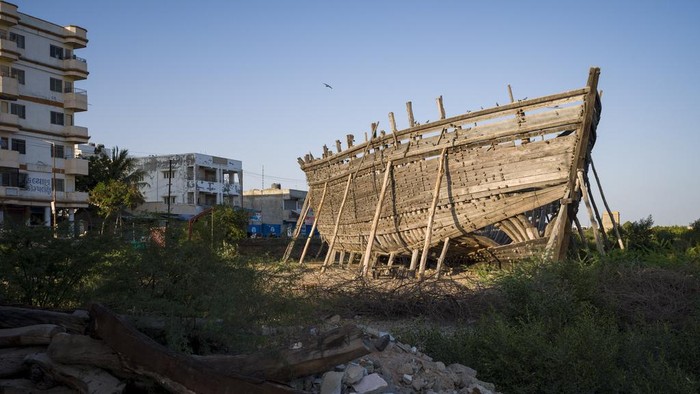Dogs sleep next to a discarded boat in the foreground at a site where two traditional ships are under construction in Mandvi in Gujarat, India, Tuesday, Jan. 9, 2024. This 400-year-old tradition of shipbuilding using manual tools is in decline but a few ships are still built each year to be used for fishing and transporting goods. (AP Photo/Ashwini Bhatia)