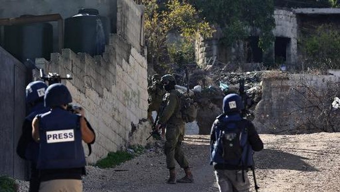 An Israeli soldier takes aim from behind a wall as journalists cover their patrol in the Jenin refugee camp, in the occupied West Bank on November 29, 2023, during an ongoing military operation in the camp. (Photo by Zain JAAFAR / AFP)