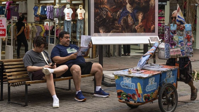 A popsicle vendor pushes his cart past a replica of The Adoration of the Magi by Pedro Pablo Rubens that is part of an outdoor exhibit organized by the Prado Museum, in downtown Montevideo, Uruguay, Tuesday, Jan. 9, 2024. (AP Photo/Matilde Campodonico)