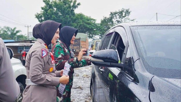 Kasat Lantas Polres Rohil, Iptu Zahratul Aulia Harun bersama Danramil 02/TanahPutih, Lettu Cba (K) Karnilawati mengatur lalu lintas dan membagikan brosur sosialisasi pemilu ke pengendara di jalan lintas yang terendam banjir di Rohil. (Dok Satlantas Polres Rohil)