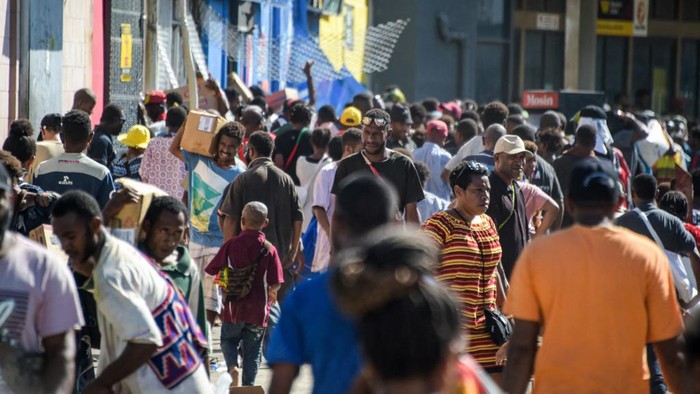 People carry items as crowds leave shops with looted goods amid a state of unrest in Port Moresby on January 10, 2024. A festering pay dispute involving Papua New Guineas security forces on January 10 sparked angry protests in the capital, where a crowd torched a police car outside the prime ministers office. By Wednesday afternoon pockets of unrest had spread through the capital Port Moresby, with video clips on social media showing crowds looting shops and stretched police scrambling to restore order. (Photo by Andrew KUTAN / AFP)