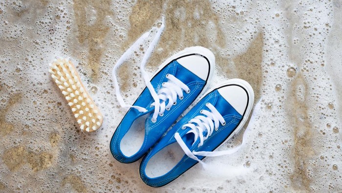 Sneakers with foam of powder detergent water dissolution and wooden brush on cement floor. Washing dirty shoes. Top view