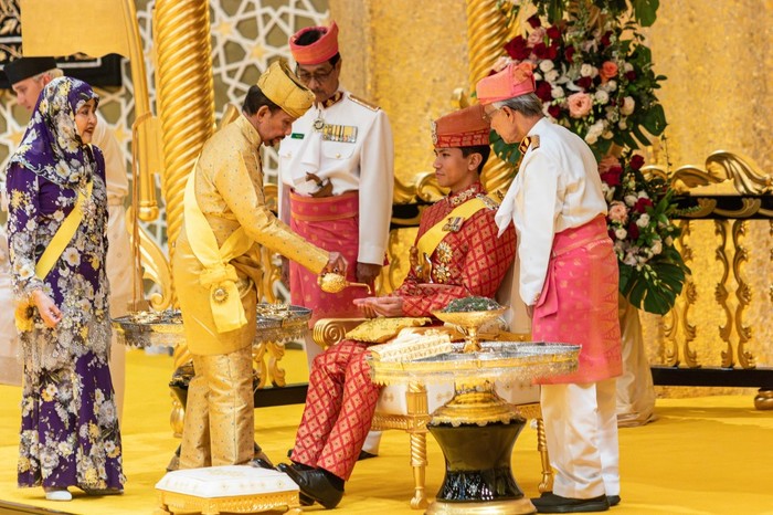 This photograph taken on January 10, 2024 shows Brunei's Sultan Hassanal Bolkiah (2nd L) pouring scented oil on the hands of Prince Abdul Mateen during the royal powdering ceremony at Istana Nurul Iman, ahead of his wedding to Anisha Rosnah, in Bandar Seri Begawan, as Queen Raja Isteri Pengiran Anak Hajah Saleha (L) looks on. Brunei's polo-playing Prince Abdul Mateen, one of Asia's most eligible bachelors, married his commoner fiancee on January 11 as part of a lavish 10-day celebration in the oil-rich sultanate. (Photo by RUDOLF PORTILLO / AFP)