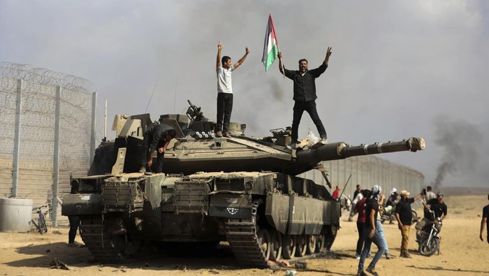 100 Hari Mencekam Genosida Israel di Jalur Gaza Palestinians wave their national flag and celebrate by a destroyed Israeli tank at the southern Gaza Strip fence east of Khan Younis on Saturday, Oct. 7, 2023. (AP Photo/Yousef Masoud)