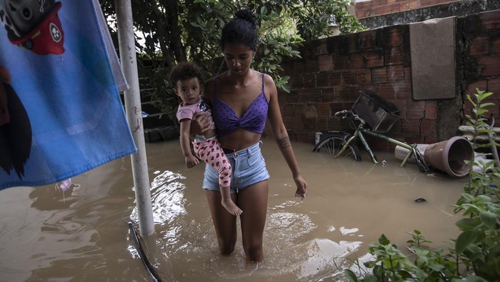 Brazil Floods Ingrid Monteiro carries her one-year-old daughter Aylla Perola over floodwaters outside their home after deadly, heavy rainfall in Duque de Caxias, Brazil, Sunday, Jan. 14, 2024. (AP Photo/Bruna Prado)