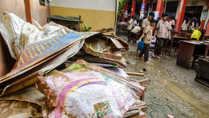 Guru membantu murid berjalan di atas kursi untuk menghindari lumpur dampak banjir di SDN Leuwi Bandung 01, Dayeuhkolot, Kabupaten Bandung, Jawa Barat, Senin (15/1/2024). Sejumlah sekolah di kawasan Kabupaten Bandung belum melaksanakan kegiatan belajar mengajar secara optimal akibat banyaknya fasilitas dan buku pedoman pelajaran yang rusak terdampak banjir beberapa waktu lalu. ANTARA FOTO/Novrian Arbi/nym.