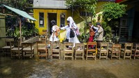 Guru membantu murid berjalan di atas kursi untuk menghindari lumpur dampak banjir di SDN Leuwi Bandung 01, Dayeuhkolot, Kabupaten Bandung, Jawa Barat, Senin (15/1/2024).