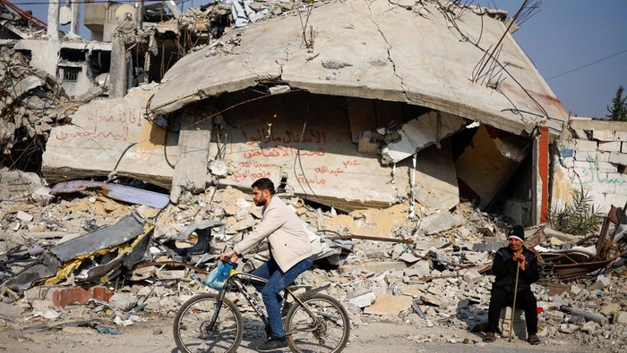 Ziad Mansour, a neighbour of the Abu Aweidah family, sits next to writing painted on a wall amid the rubble of the familys house, which was destroyed in a deadly Israeli strike amid the ongoing conflict between Israel and the Palestinian Islamist group Hamas, in Rafah, Gaza Strip, January 9, 2024. REUTERS/Mohammed Salem