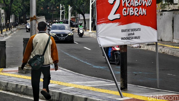 Baliho Capres-Cawapres Serobot Jalur Pedestrian Pejalan kaki menghindari Alat Peraga Kampanye (APK) yang terpasang di jalur pedestrian di Jl Cemara, Jakarta Pusat, Selasa (16/1/2025). Pemasangan APK yang menyerobot trotoar itu dikeluhkan warga seperti terekam dalam akun instagram koalisi pejalan kaki. APK dinilai merampas hak pejalan kaki dan merusak fungsi trotoar.