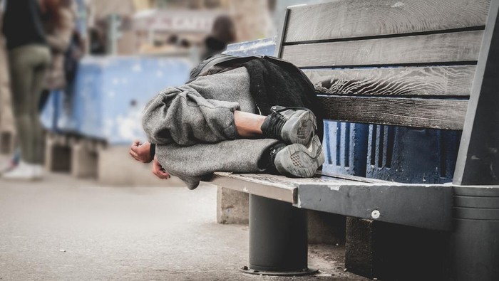 Senior man homeless wearing sweater and cloth gloves with sitting on cardboard and tying laces on shoes. Close up of asian man homeless in shelter and wear leather shoes boot and tie lace his shoes.