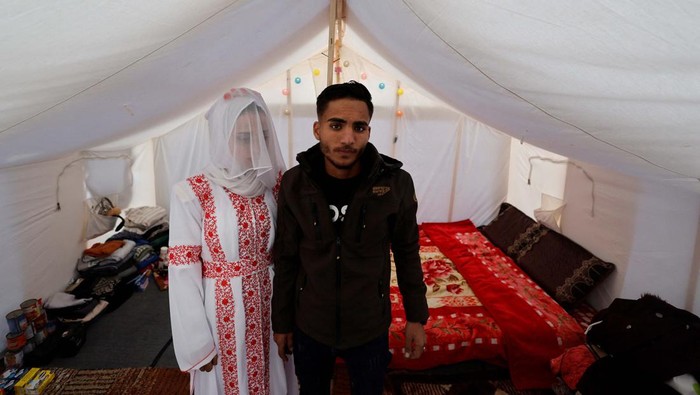 Pernikahan Sederhana Warga Gaza di Pengungsian A Palestinian couple stands in a tent camp, amid the ongoing conflict between Israel and the Palestinian Islamist group Hamas, on their wedding day, in Rafah in the southern Gaza Strip, January 18, 2024. REUTERS/Mohammed Salem