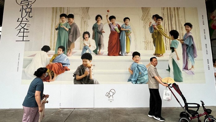 A man pushes a stroller and a woman holds a child as they walk past a billboard in Shenzhen, Guangdong province, China April 21, 2023. REUTERS/David Kirton/File Photo