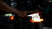 Arifin sedang menempah lonjoran besi yang merah merona untuk dibentuk menjadi pisau dan juga sabit untuk pertanian.