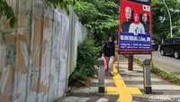 Warga melintasi jalur pedestrian dengan Alat Peraga Kampanye (APK) yang menyerobot guiding block atau jalur petunjuk tuna netra, di sejumlah jalur pedestrian di Jakarta, Rabu (24/1/2024).
