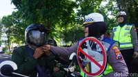 Petugas Polantas membantu pengguna jalan yang tidak memakai helm dengan benar.