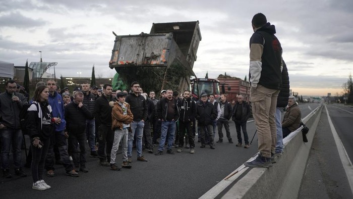 Protes Aturan dan Upah, Petani di Prancis Blokir Jalan dengan Traktor Farmers listen to a speech as they block the M6 motorway near Lyon, central France, Wednesday, Jan. 24, 2024. French farmers protest across the country and in Brussels against low wages and what they consider to be excessive regulation, mounting costs and other problems. (AP Photo/Laurent Cipriani)