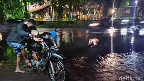 Pengendara bernama Victor mencoba menyalakan sepeda motornya yang mogok akibat banjir di Jalan Raya Puputan, Kota Denpasar, Bali, Sabtu (27/1/2024).