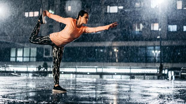 1467930949 Beautiful young athletic woman stretching before jogging outdoors in the rain at night.