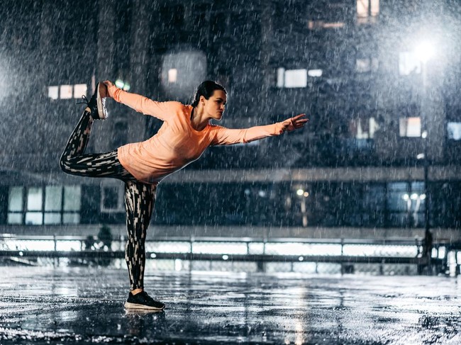 Beautiful young athletic woman stretching before jogging outdoors in the rain at night.