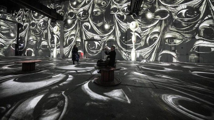 Visitors watch digital multimedia artworks projected on the walls of a former steelworks featuring Spanish surrealist artist Salvador Dali at the Phoenix des Lumieres, located in a former puddling and rolling mill, in Dortmund, Germany, Thursday, Jan. 25, 2024. (AP Photo/Martin Meissner)