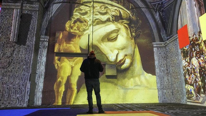 Visitors watch digital multimedia artworks projected on the walls of a former steelworks featuring Spanish surrealist artist Salvador Dali at the Phoenix des Lumieres, located in a former puddling and rolling mill, in Dortmund, Germany, Thursday, Jan. 25, 2024. (AP Photo/Martin Meissner)
