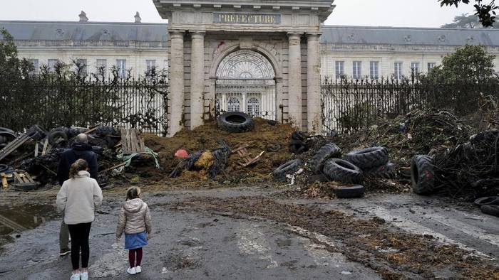 Gedung Pemerintah Prancis Dipenuhi Sampah Imbas Protes Petani People watch slurry, manure and tyres dumped by farmers at the entrance of the local state administration building, in Agen, southwestern France, Saturday, Jan. 27, 2024. French farmers have vowed to continue protesting and are maintaining traffic barricades on some of the country's major roads. The government announced a series of measures Friday but the farmers say these do not fully address their demands. (AP Photo/Fred Scheiber)